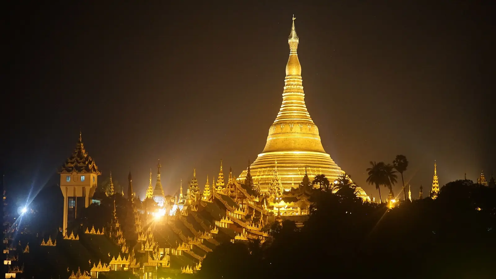 The illuminated golden spire of the Shwedagon Pagoda and its surrounding shrines glowing against the night sky