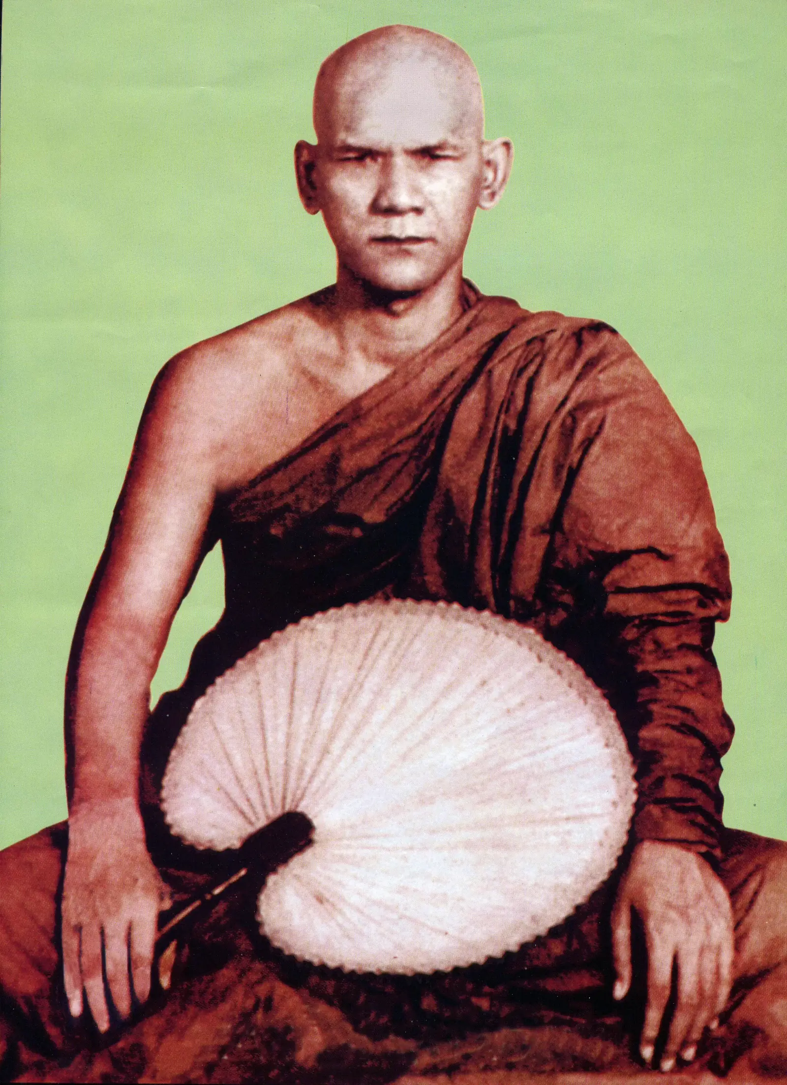 Hand-tinted portrait photograph of Mahasi Sayadaw seated in maroon robes, holding a round palm-leaf fan